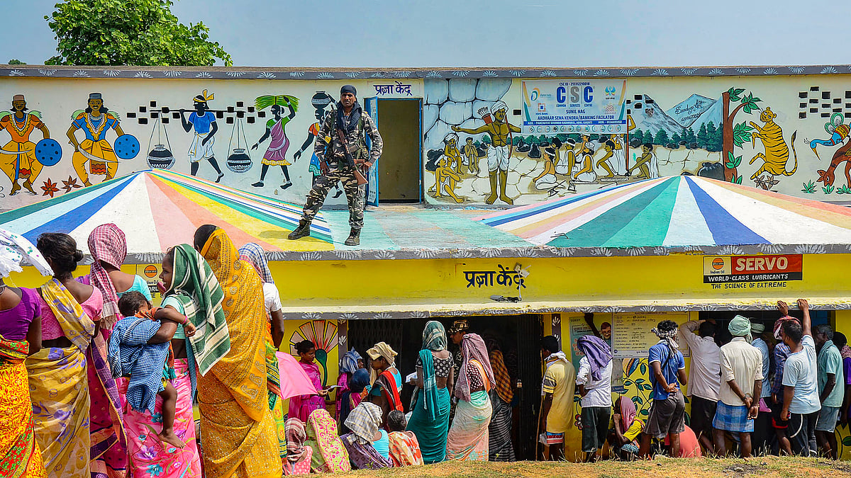 A security personnel stands guard as voters wait at a polling station in Khunti, Jharkhand (photo: PTI)