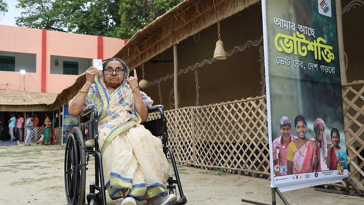 A disabled woman shows off her inked finger and ID card after casting her vote in Malda, West Bengal; a poster beside her says 'I have the voting power; I will vote, I will build my nation' (photo courtesy @CEOWestBengal/X)