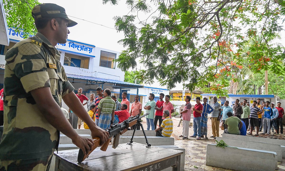 A BSF jawan stands guard as people queues outside a polling booth in Hooghly district, West Bengal (photo: PTI)