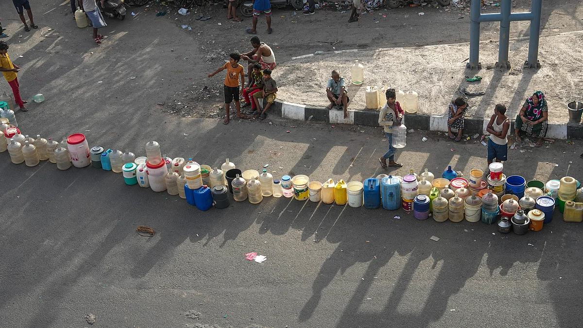 People wait to collect drinking water from a tanker of Delhi Jal Board at a slum in East Delhi