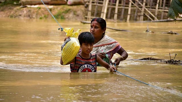 Mother and child wade in chest-deep water with precious essentials held aloft (photo: @abuasimazmi/X)