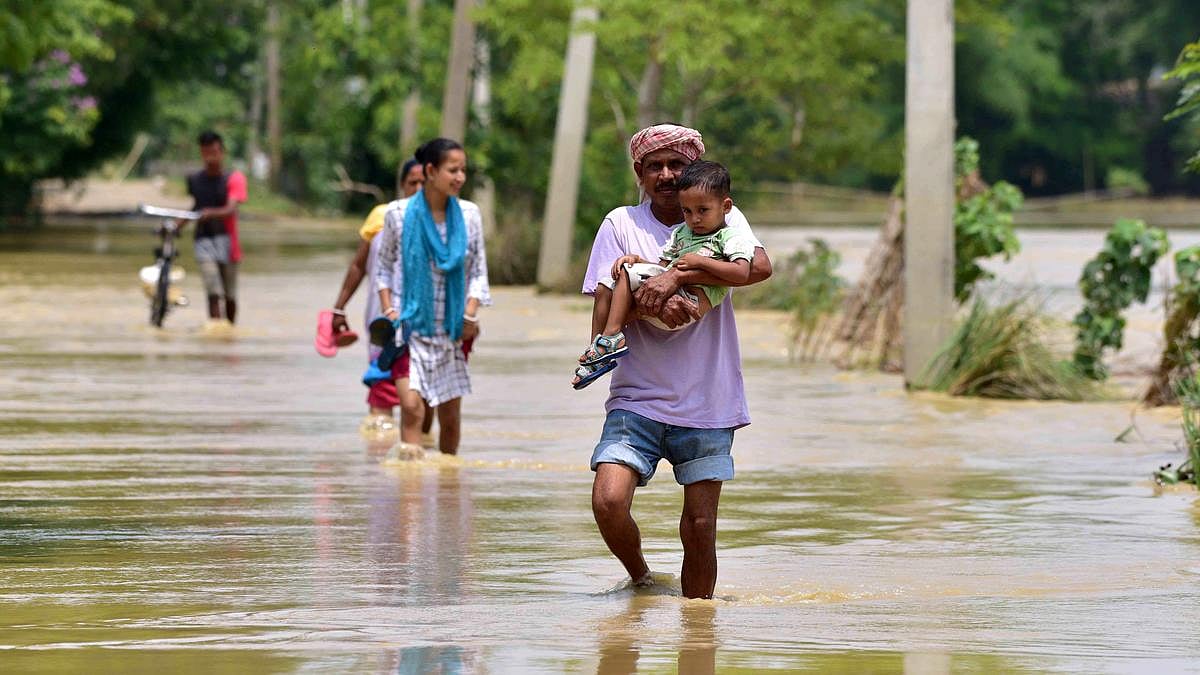 A man carries a small child as he wades through flood waters in Assam (photo: @abuasimazmi/X)