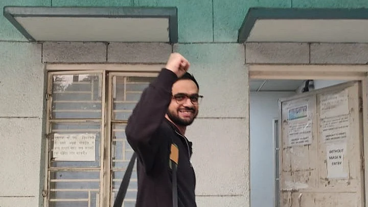 Umar Khalid walks back into jail after a transit bail, smiling, hand upheld in a closed fist salute