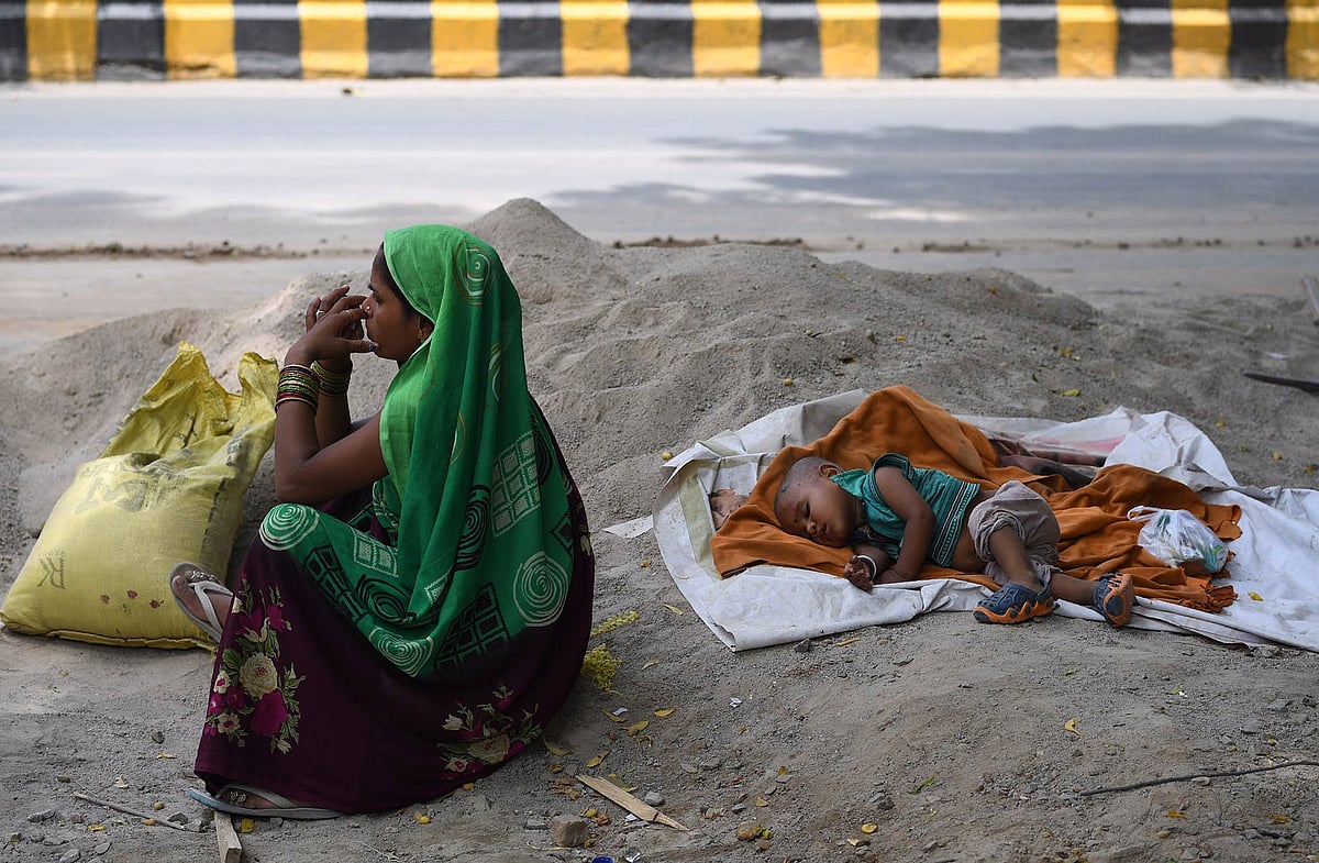 A construction worker sits by the roadside, her infant asleep in a cement heap (@sajjadkmr/X)