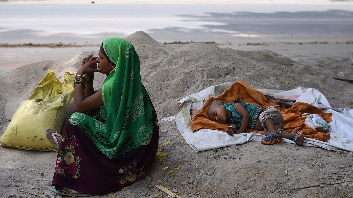 A construction worker sits by the roadside, her infant asleep on a cement heap