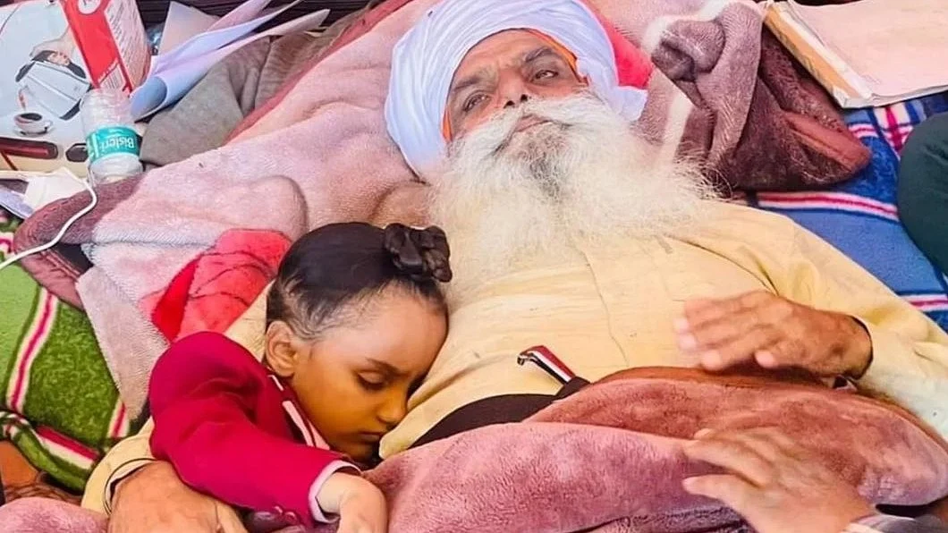 BKU leader Jagjit Singh Dallewal, on a fast unto death, cuddles a young relative asleep at his side