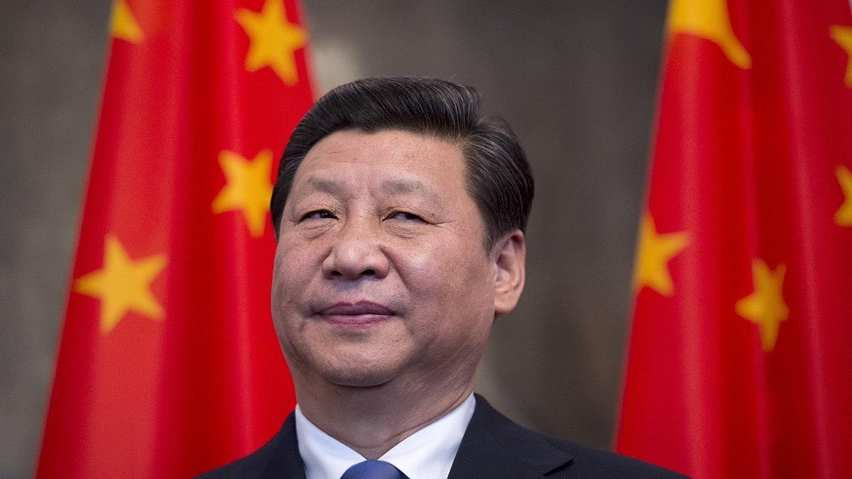 China's president Xi Jinping smiles, with an apparent side-eye, before a row of Chinese national flags