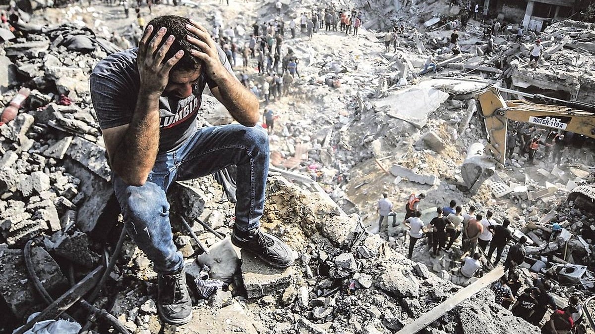 A man in Gaza sits atop the rubble in despair, others dig (image courtesy @YusufCatStevens/X)
