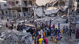 Palestinians collect water from a truck amidst devastation in Gaza City.