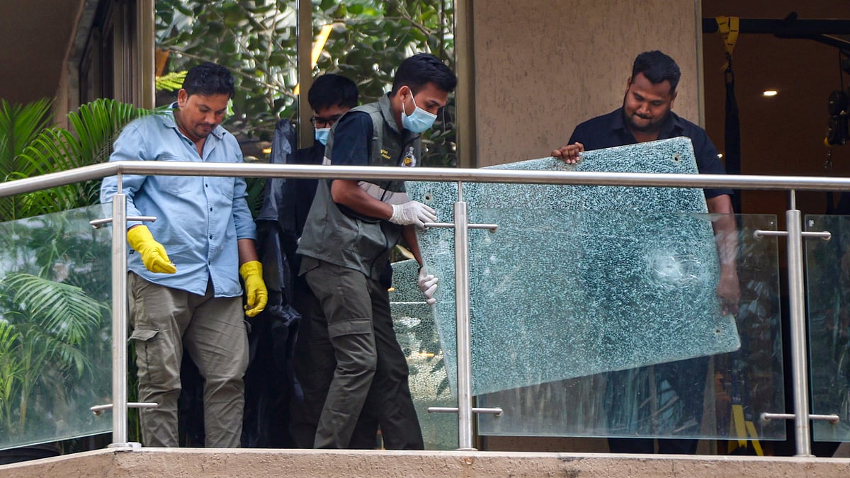 Forensic team members remove a shattered glass pane from the balcony of Rohit Shetty's residence.