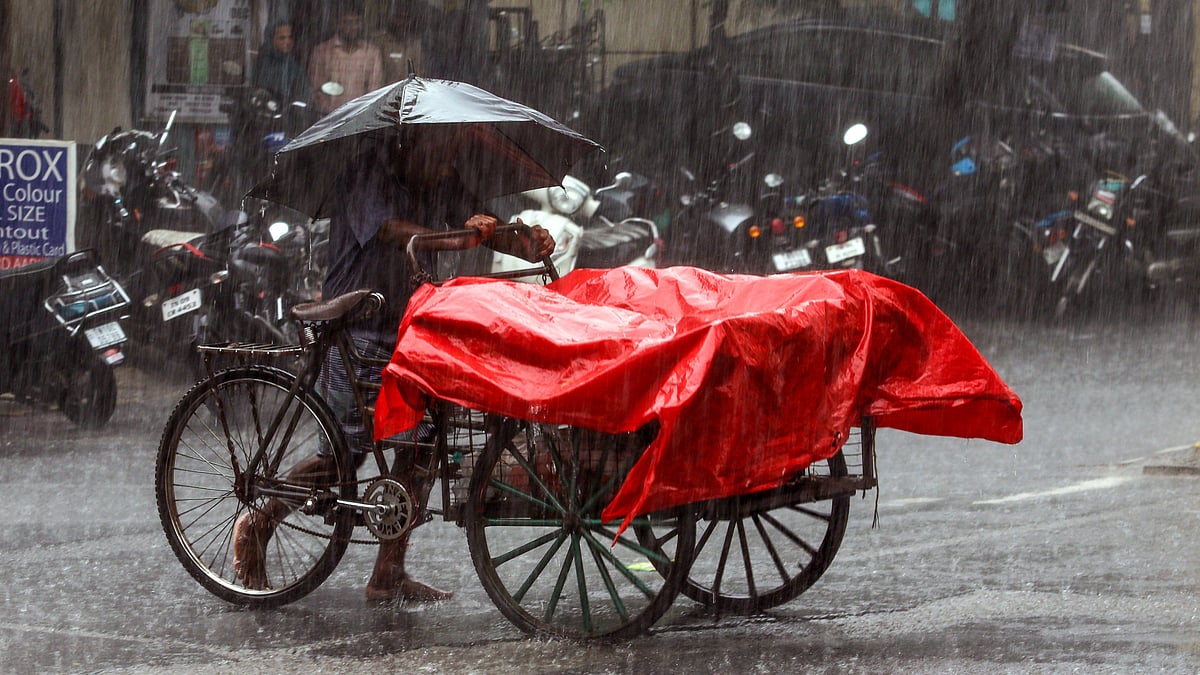 A street vendor shields himself and his cart from heavy rain on a drenched Chennai street.