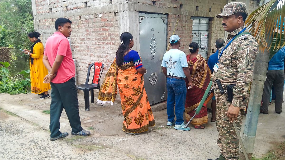 A security official stands guard as voters queue up during Falta repoll in West Bengal.