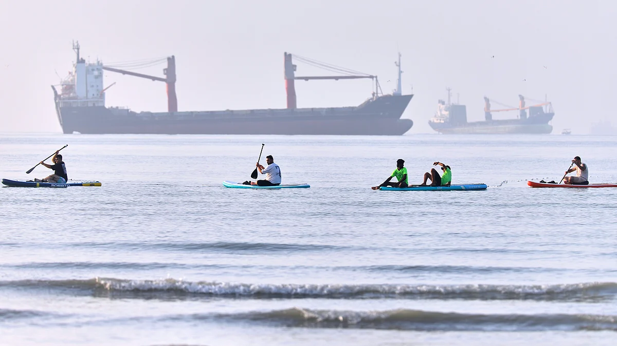 People paddle along the shoreline with cargo ships anchored in the Strait of Hormuz, 1 June
