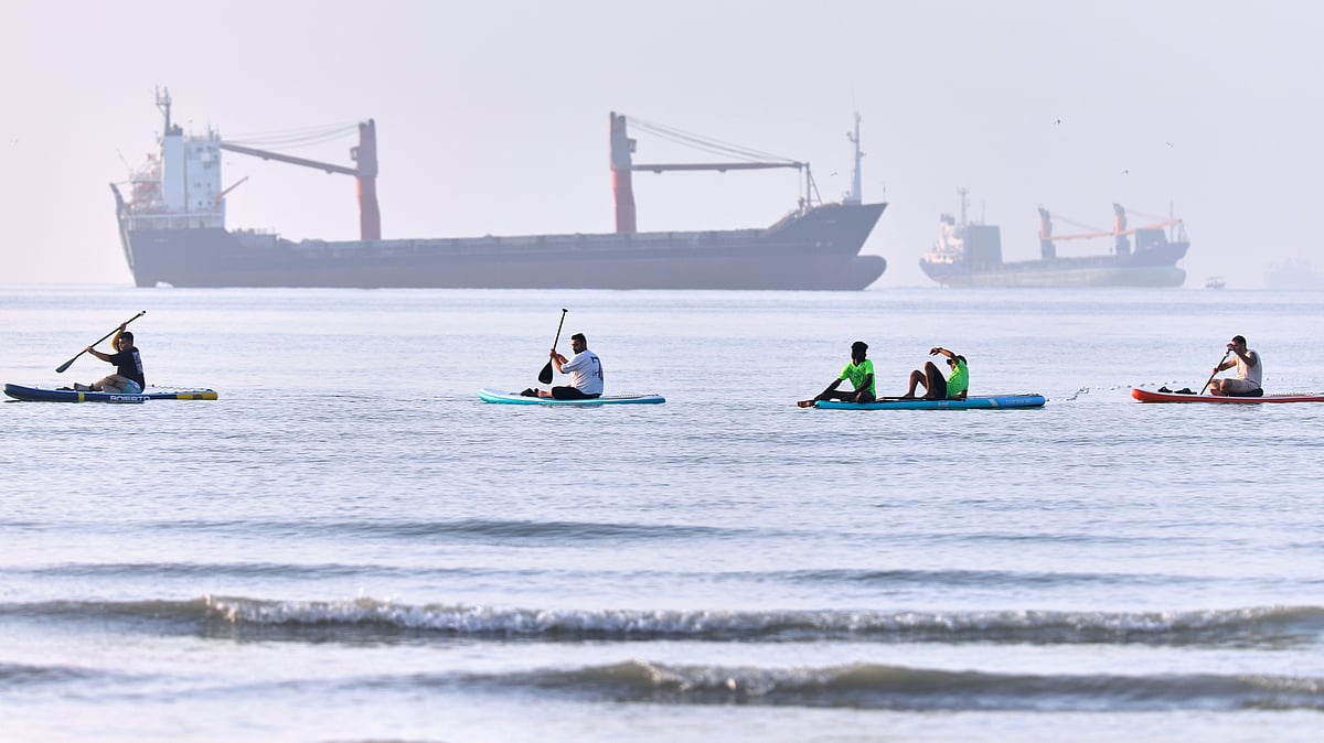 People paddle along the shoreline with cargo ships anchored in the Strait of Hormuz, 1 June