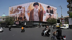 Motorcycles drive past a billboard showing the late Iranian Supreme Leader Ayatollah Ali Khamene