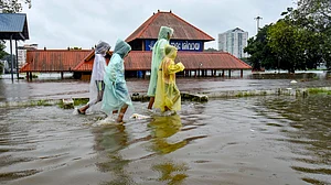 Children cover themselves as they move on a waterlogged road following rainfall in Kochi.