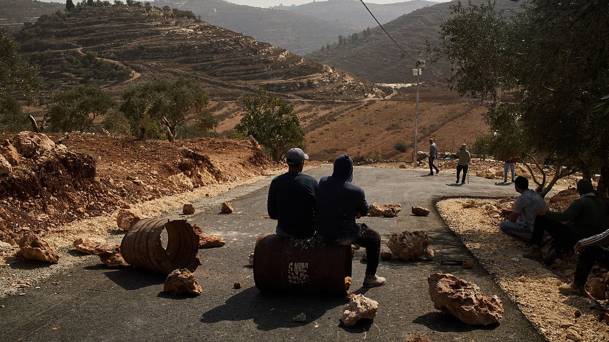 Palestinian men sit along a road blocked to prevent Israeli settlers from entering the area.