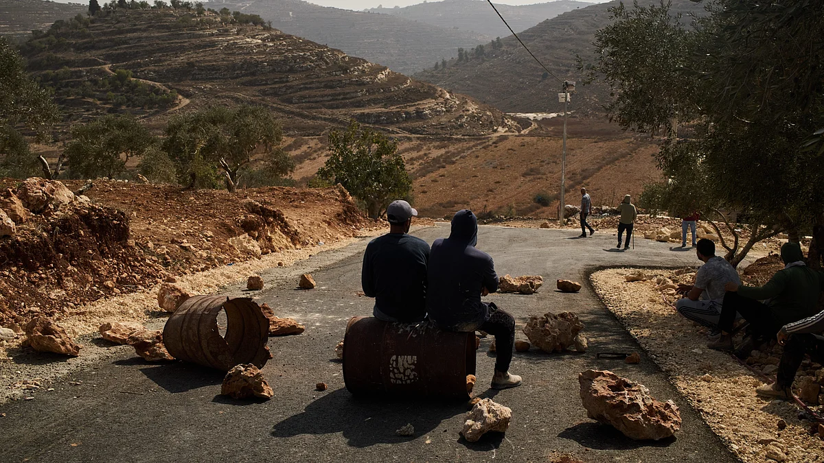 Palestinian men sit along a road blocked to prevent Israeli settlers from entering the area.