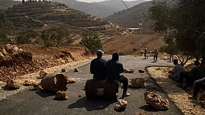Palestinian men sit along a road blocked to prevent Israeli settlers from entering the area.