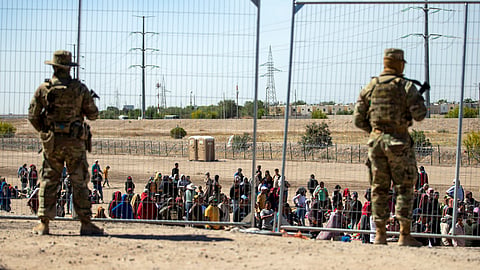Migrants wait in line adjacent to the border fence under the watch of the Texas National Guard to enter into El Paso, Texas, May 10, 2023. 