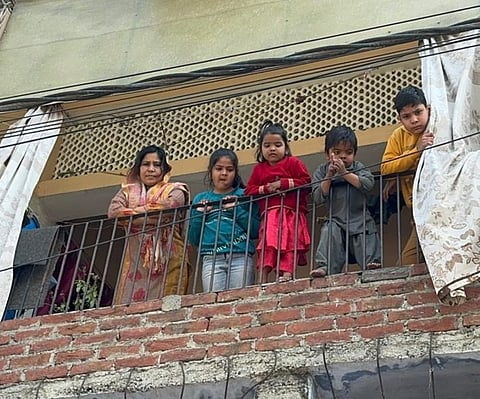 In the curfew-bound neighborhood of Banbhulpura, young children observe the streets with curiosity, from their home's balcony.
