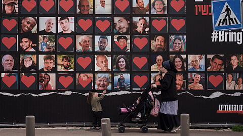 A woman and her children walk past a wall with photographs of hostages who were kidnapped during the Oct. 7 Hamas cross-border attack in Israel in Jerusalem.