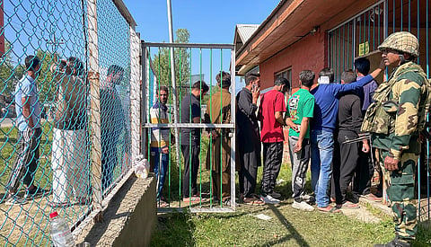 A security personnel stands guard as voters wait in a queue at a polling station to cast their votes for the fifth phase of Lok Sabha elections, in Sopore, Monday, May 20, 2024. People come out in large numbers in Sopore in North Kashmir, once known as a hot bed of militancy. 