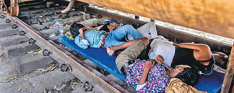 Roadside vendors rest in the shade beneath a stationary train coach on a hot summer day in Mumbai 