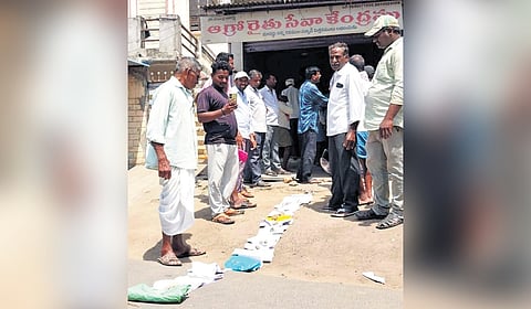 Farmers in Jagtial leave their passbooks and sandals in line to hold their place while they stand nearby on Wednesday