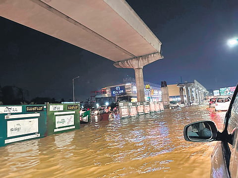 Cars slowly make their way on the New Airport Road, near Chikkajala, which got waterlogged, causing hurdles for traffic movement, in Bengaluru on Thursday