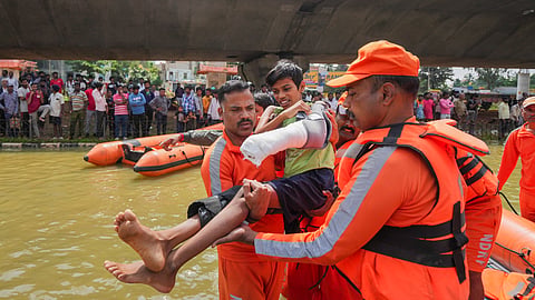 NDRF personnel carry a boy with a plaster cast on his arm as they conduct rescue operations after floodwater entered the Kendriya Vihar apartment following heavy rain, in Bengaluru.