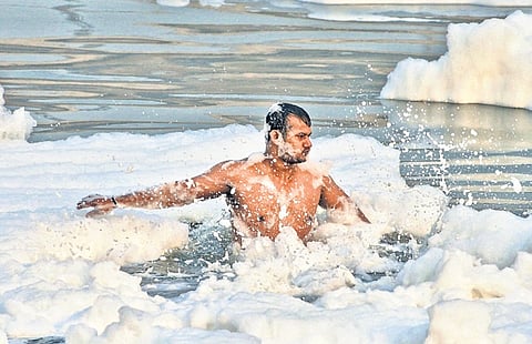 A devotee takes a holy dip in Yamuna as toxic foam floats during the start of the 4-day Chhath Puja at Kalindi Kunj on Tuesday