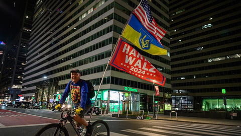 A cyclist rides across a street flying a Ukrainian flag and another supporting US democratic presidential candidate Kamala Harris in central Philadelphia, on November 4, 2024, ahead of election day.