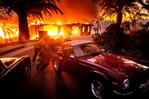 Firefighters and sheriff's deputies push a vintage MG away from a burning home as the Mountain Fire burns in Camarillo, Calif., on Wednesday, Nov. 6, 2024. 