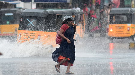 Pedestrians shield themselves with makeshift covers while wading through heavy rain at Anna salai  in Chennai