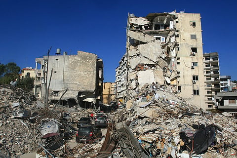 People drive past buildings, destroyed during the war between Hezbollah and Israel, in the southern Lebanese city of Nabatieh on December 1, 2024. 