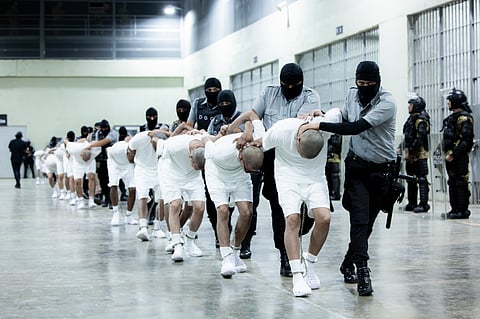 In this photo provided by El Salvador's presidential press office, prison guards transfer deportees from the US, alleged to be Venezuelan gang members, to the Terrorism Confinement Center in Tecoluca, El Salvador.