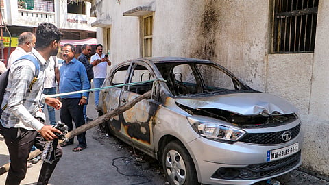 People stand near charred remains of a car at Chitnis Park area amid curfew after violence erupted on Monday night.