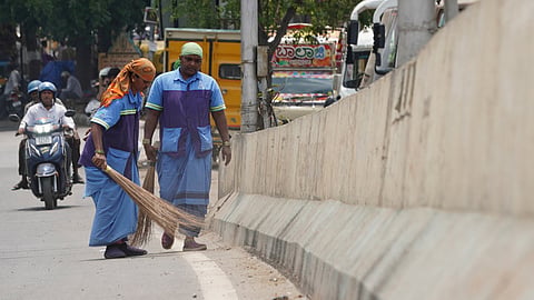 Civic workers seen cleaing the road during the sunny weather at Outer ring road in Bengaluru. 