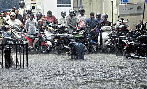 A man tries to clear the blockage at a manhole as commuters 
wait for the very heavy rain that lashed Hyderabad on Friday to 
subside.