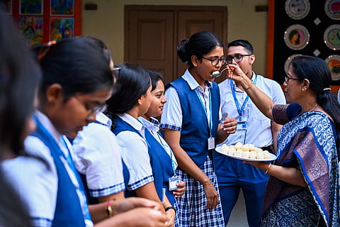A teacher distributes sweets to students for passing CBSE plus two exams with flying colours at BJEM School in Bhubaneswar on Tuesday. 