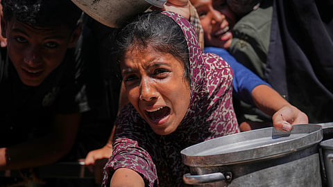 Palestinians struggle to receive cooked food distributed at a community kitchen in the Muwasi area of Khan Younis, in the Gaza Strip, Friday, May 23, 2025. 