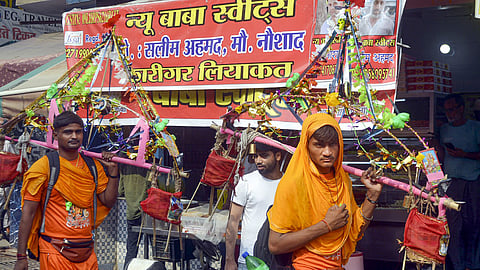 Kanwariyas walk past a shop on which banners with shopkeeper's name was put up on Kanwar Marg after an order issued by Uttar Pradesh Government, in Muzaffarnagar, Saturday, July 20, 2024. 