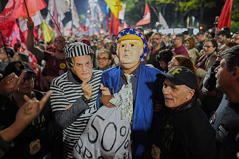 Protesters wearing masks of U.S. President Donald Trump and former President Jair Bolsonaro as a prisoner, protest Trump's announcement of 50% tariffs on Brazilian goods, in Sao Paulo, Thursday, July 10, 2025.
