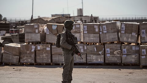 An Israeli soldier stands beside humanitarian aid packages awaiting pickup on the Palestinian side of the Kerem Shalom crossing in the Gaza Strip, Thursday, July 24, 2025. during a media tour organized by the Israeli army. 