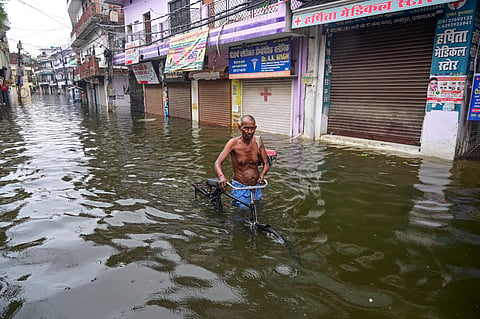 A man with his bicycle makes his way through a waterlogged area following rainfall, in Prayagraj, Uttar Pradesh, on Monday