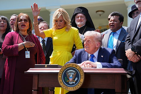  President Donald Trump sits at a desk as he and religious leaders listen to a musical performance before Trump signs an executive order during a National Day of Prayer event in the Rose Garden of the White House, May 1, 2025, in Washington.