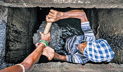 A sanitation worker handing over silt from a drain to another worker, both without any protective gear like gloves and masks in Bhubaneswar 
