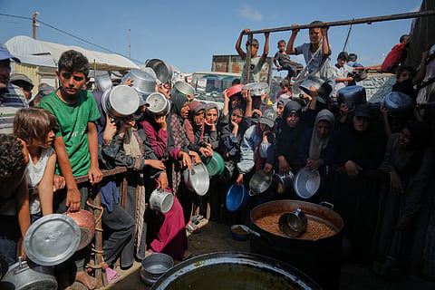 Palestinians wait to get donated food at a community kitchen in Khan Younis, southern Gaza Strip, Sunday, Oct. 5, 2025. 