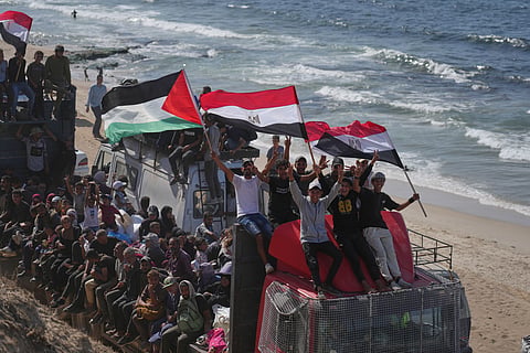 Displaced Palestinians ride on trucks loaded with belongings and wave Egyptian and Palestinian flags as they travel along the coastal road near Wadi Gaza in the central Gaza Strip, moving toward Gaza city, Saturday, Oct. 11, 2025, after Israel and Hamas agreed to a pause in their war and the release of the remaining hostages. 